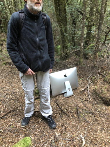 man in woods, iMac resting by his foot